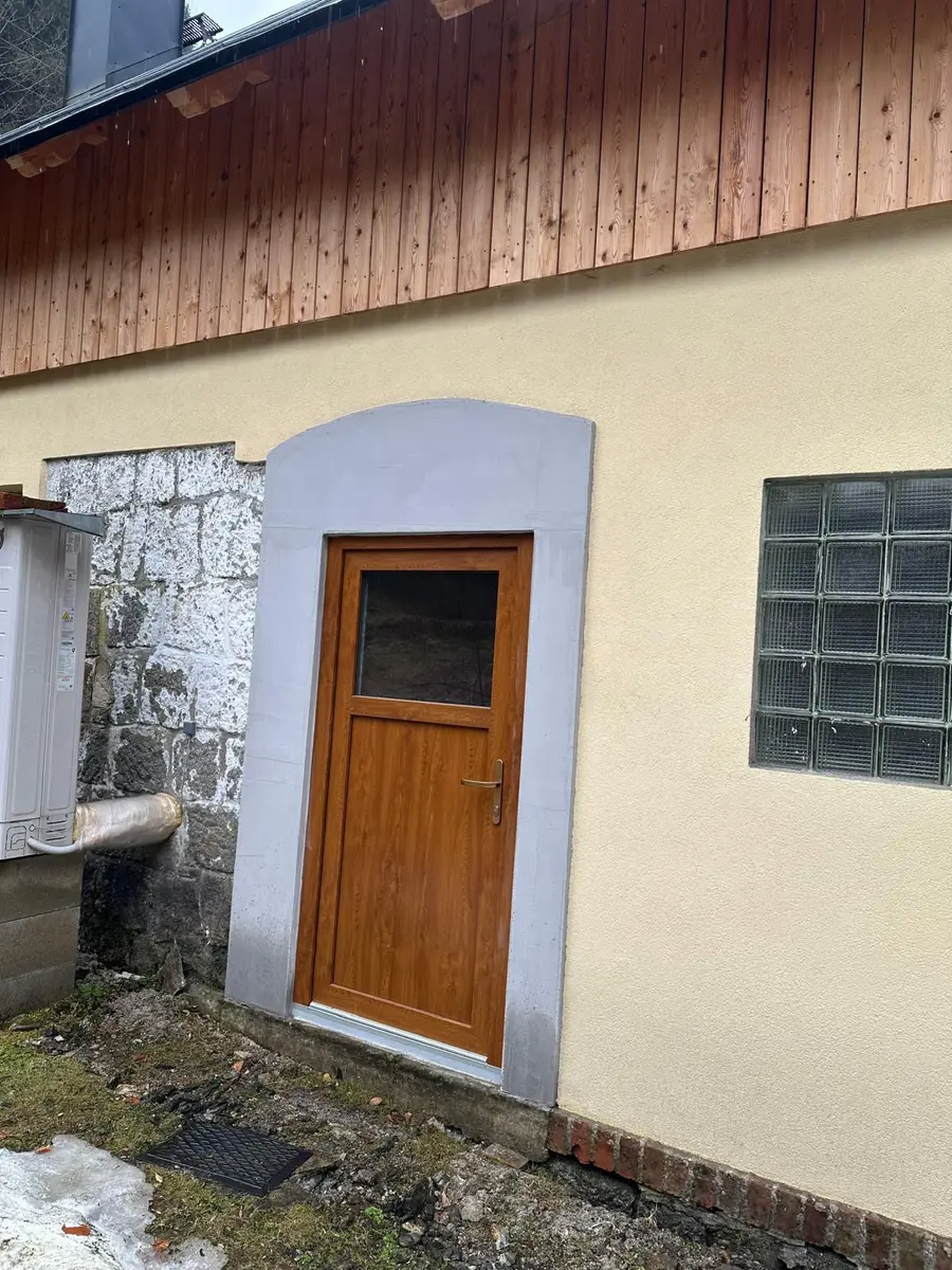 Dokončená fasáda domu se dřevěným obkladem, vchodovými dveřmi a skleněnými tvárnicemi